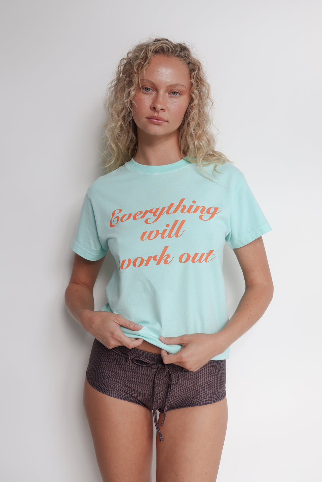 Person wearing a aqua t-shirt with 'Everything will work out' text in orange.