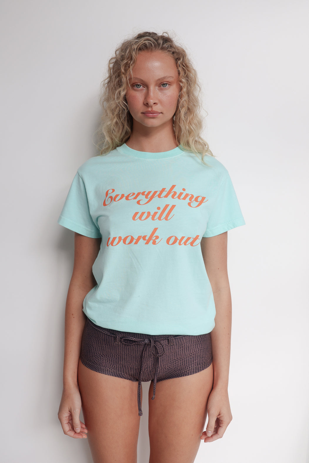 Person wearing a aqua t-shirt with 'Everything will work out' text in orange.