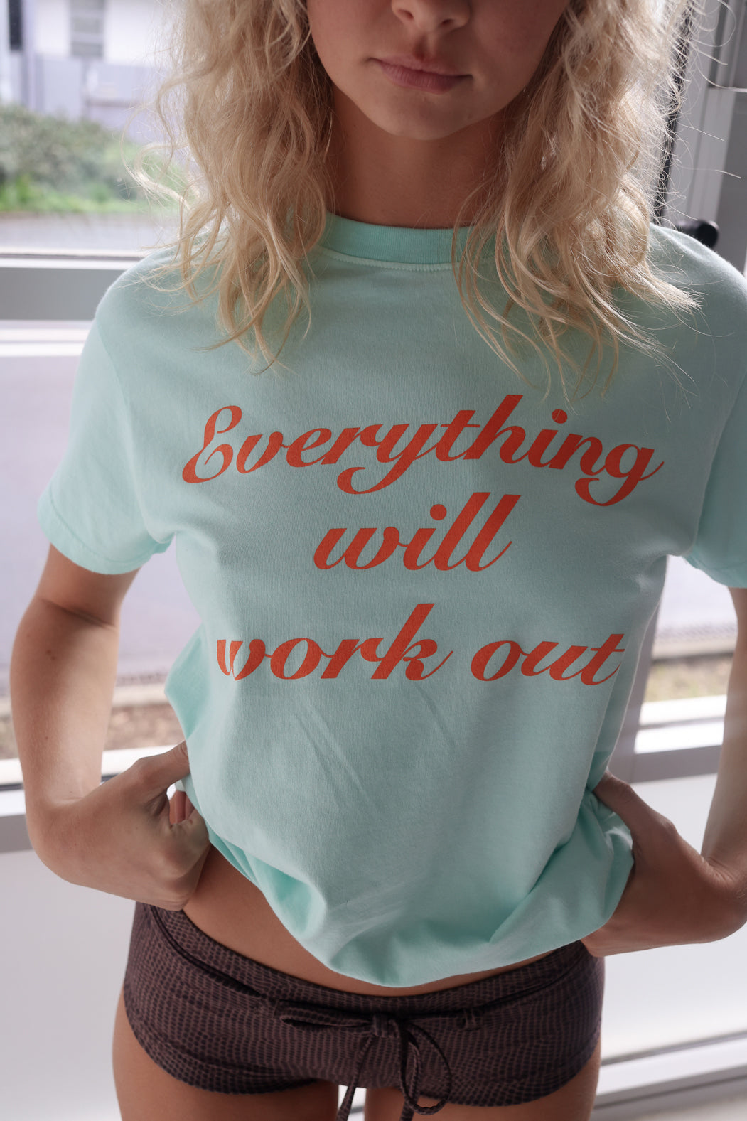 Person wearing a aqua t-shirt with 'Everything will work out' text in orange.
