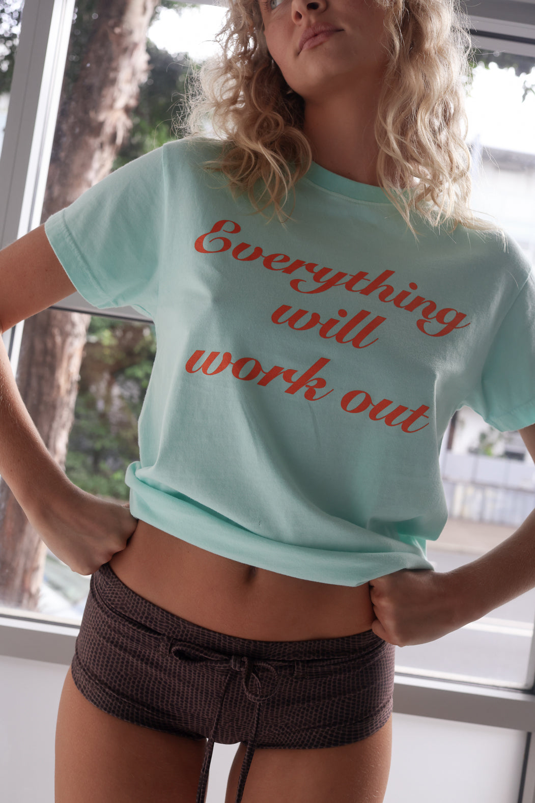 Person wearing a aqua t-shirt with 'Everything will work out' text in orange.