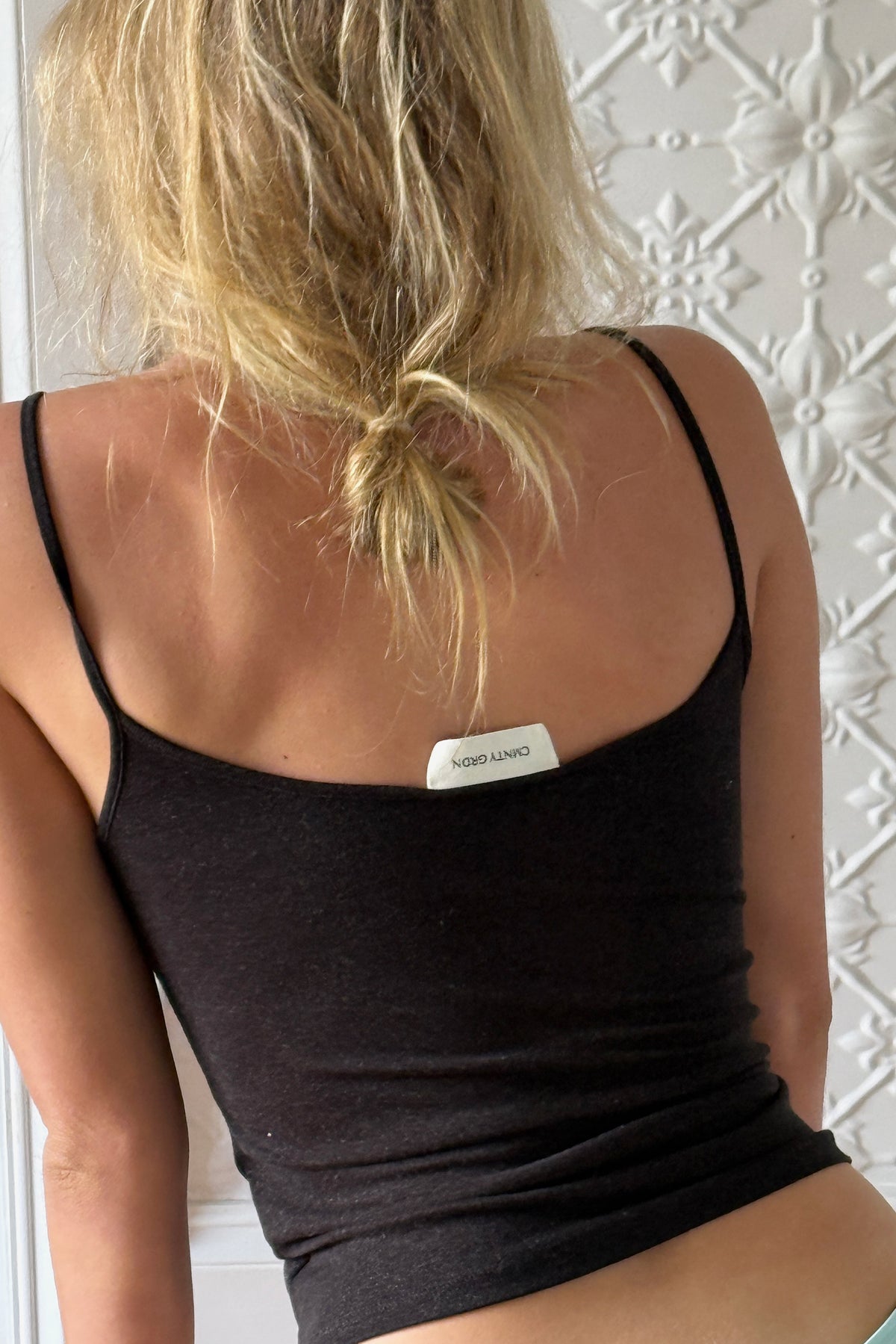 Blonde model wearing a black singlet top against a white textured wall